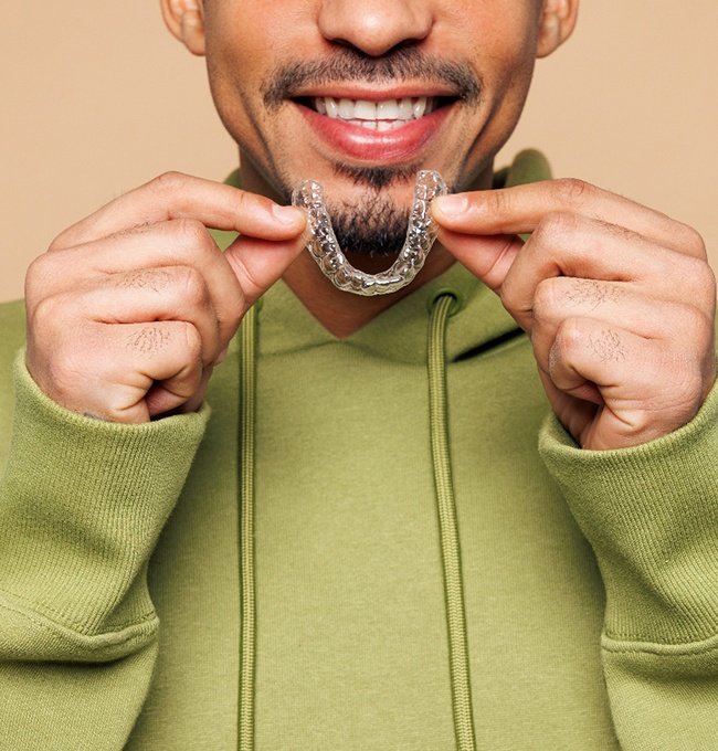 Man smiling while holding Invisalign tray 