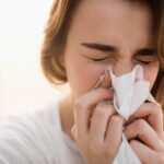 person suffering from seasonal allergies blowing nose